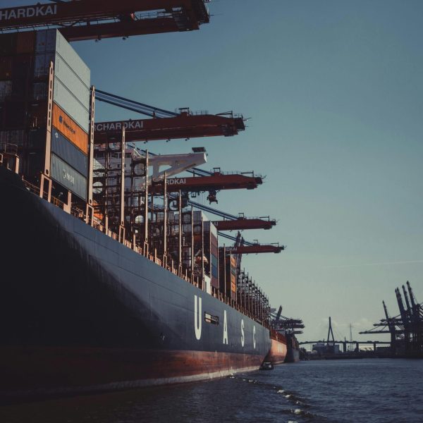 A large cargo ship docked at Hamburg Harbor, cranes loading containers under a clear sky.