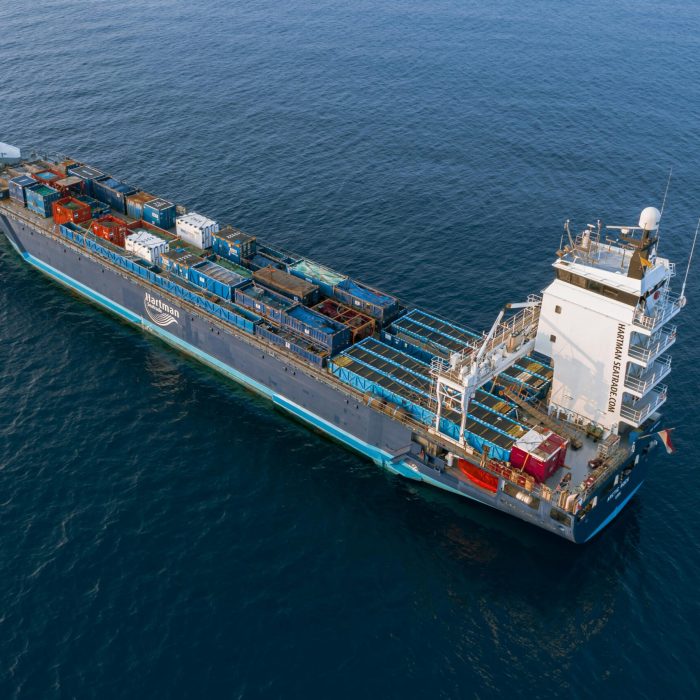 A drone captures a vibrant container ship navigating deep blue ocean waters.